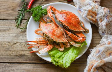 Lokantada beyaz tabakta taze deniz ürünleri pişiyor, haşlanıyor ya da haşlanıyor mavi yüzme yengeci okyanus gurmesi acılı bitki ve baharatlı limon ve biberiye ile ahşap yemek masasında. 