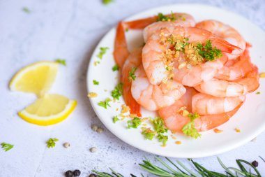 Taze karides, karides, baharatlı deniz mahsulü limon, arka planda beyaz tabak üzerine soyulmuş sarımsaklı karides, yemek masası.