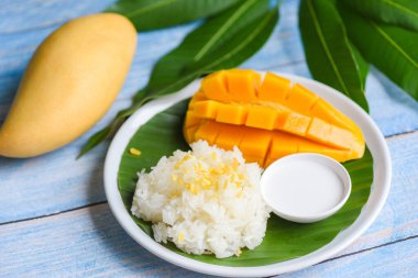 Hindistan cevizi sütüyle pişirilmiş olgun mango pilavı, Asya Tayland tatlısı tropik tatlı mango kabuğu ve beyaz tabakta dilimlenmiş taze mango yaprağı, mango yapışkan pirinç yaz meyvesi