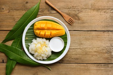 Tayland usulü tatlı mango kabuğu ve beyaz tabakta dilimlenmiş taze mango, hindistancevizi sütüyle pişirilmiş olgun mango pilavı ve tropikal meyve yemeği.