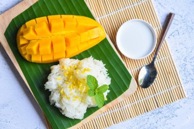 Hindistan cevizi sütüyle pişirilmiş olgun mango pilavı, yapışkan pirinç yaz tropikal meyve Asya tatlı mango kabuğu muz yaprağı ve taze nane yapraklarıyla dilimlenmiş Tayland tatlı mango kabuğu