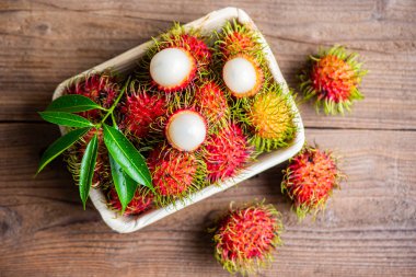 Rambutan fruit on plate and wooden background harvest from the garden, Fresh and ripe rambutan sweet tropical fruit peeled rambutan with leaves 