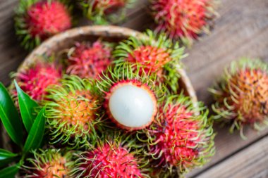 Rambutan fruit on basket and wooden background harvest from the garden, Fresh and ripe rambutan sweet tropical fruit peeled rambutan with leaves 