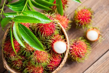 Taze ve olgun rambutan tatlı tropikal meyve yapraklı rambutan, sepette Rambutan meyvesi ve bahçeden ahşap arkaplan hasadı.
