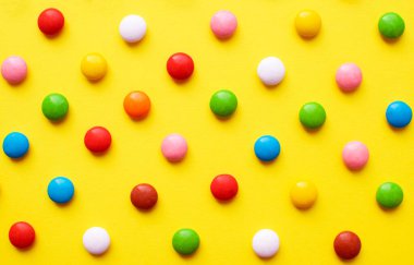 Sarı arka planda renkli şeker topları. Çikolata şekerleri çok renkli şeker jölesiyle kaplıdır.. 