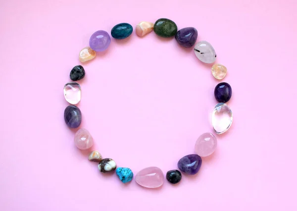 The circle is lined with natural minerals. Semi-precious stones of different colors, raw and processed. Amethyst, rose quartz, agate, apatite, aventurine on a pink background