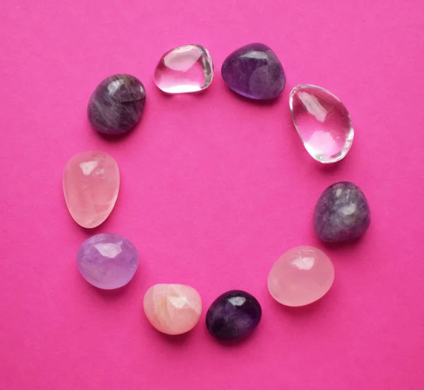 The circle is lined with natural minerals. Semi-precious stones of different colors processed. Amethyst and rose quartz. Frame of gems on bright pink background.