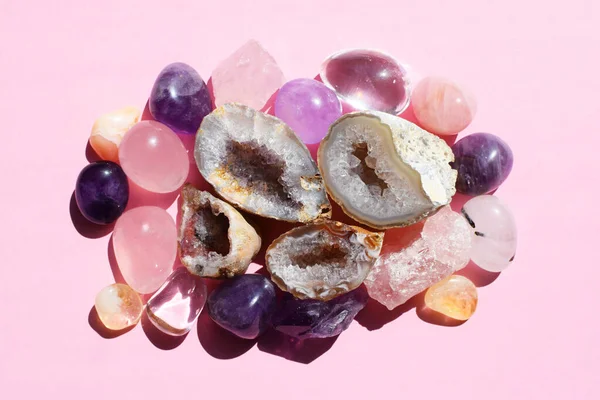 Beautiful gemstones, amethyst geode and druze of natural purple mineral amethyst on a pink background against a bright light. Amethyst and rose quartz. Large crystals of semi-precious stones.