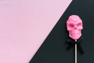 Pembe ve siyah arka planda çubuk üzerinde kafatası şeklinde lolipop. Cadılar Bayramı konsepti.