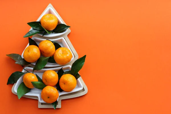 Turuncu arka planda Noel ağacı şeklinde mandalinalar. Noel yemekleri arka planı, en iyi manzara. Eğlenceli bir Noel ağacı.