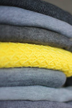 Kış için sıcak, sıcak giysiler yığını. Gri kazaklar arasında biri sarı. Giysileri sınıflandırmak, ev eşyaları düzenlemek.