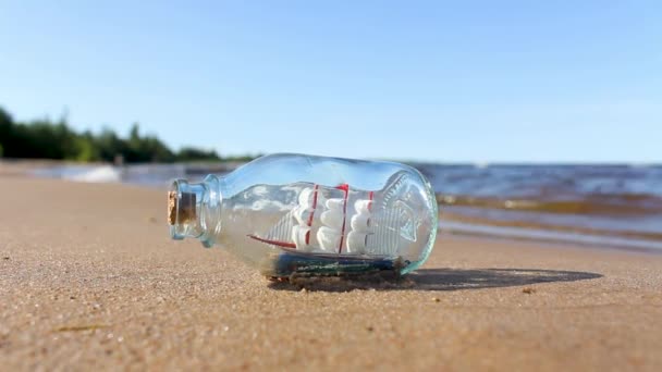 El barco en la botella está acostado en la arena cerca del agua. un recuerdo del mar. el concepto de agradables recuerdos y sueños del mar — Vídeo de stock