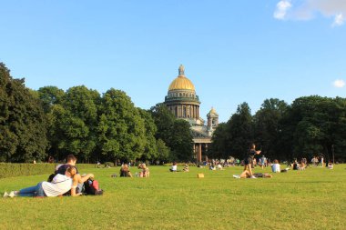 İnsanlar yazın St. Isaacs Katedrali 'nin önündeki çimlerin üzerinde dinleniyorlar. Turist Saint Petersburg