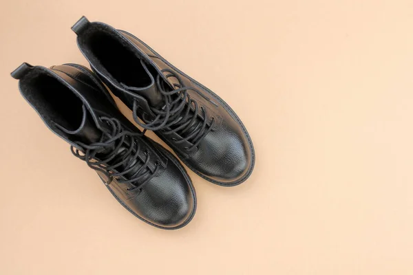 Kahverengi arka planda siyah deri çizmeler. Modern kadın ayakkabıları askeri tarzda.