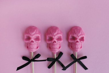 Pembe bir arka planda çubuk üzerinde kafatası şeklinde üç tane pembe lolipop. Cadılar Bayramı konsepti.