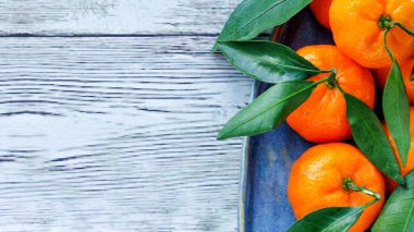 Ahşap zemin üzerinde mavi bir tabakta yaprakları olan mandalinalar. Noel yemeğinin bir sembolü, uzayın bir kopyası..