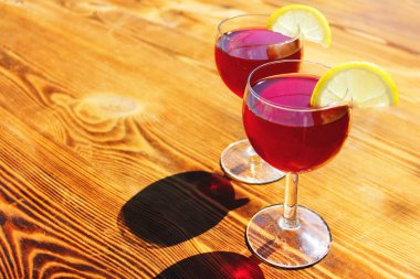 İki bardak kırmızı yaz kokteyli ve ahşap arka planda limon dilimleri.