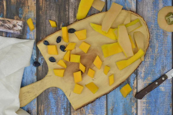 Kabak kabukları ve parçalar, tahtanın üzerinde kuru erikler, doğrama tahtası. Mutfakta hasat var. Üst manzara ahşap, mavi masa.