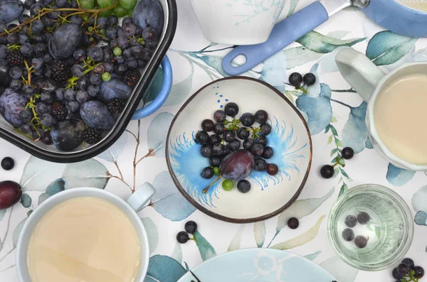 Mavi, nane, açık yeşil süslemeli koyu mavi üzümler ve erikler, mavi kızartma tavası ve kır mutfağında sütlü büyük bardaklarda kahve. Hasat et, reçel yap, meyve suyu veya kek yap.