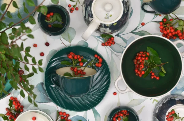 Yapraklarla boyanmış bir masa örtüsünün üzerinde yeşil masa örtüsü ve rowan üzümünden yapılmış kırmızı süslemeler. En üst düzey masa dekorasyonu örneğin özel bir durum için bir yemek odasında ya da bir restoranda..