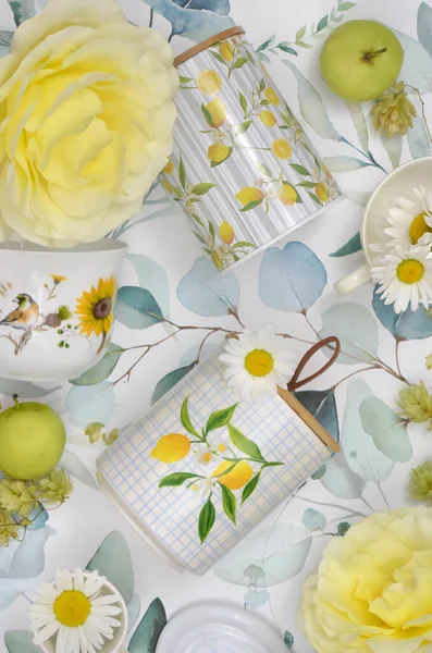 Sarı ve yeşil mutfak veya masa dekorasyonu: çiçekler, meyveler, fincanlar, depolama kapları ve kapaklar. Kır mutfağında iki renkli üst manzara dekorasyonu. 