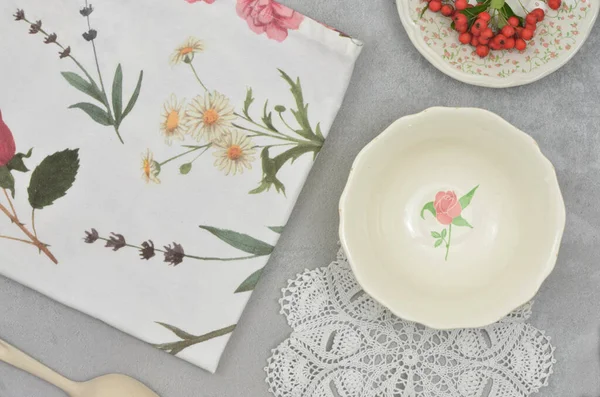 Süslü bir kâse boyalı bir gül, çiçek ve yapraklarla boyanmış mutfak havlusu, örülmüş beyaz altlık ve küçük güllerle kaplı bir tabakta Rowan çileği. Kırsal, şirin mutfak..