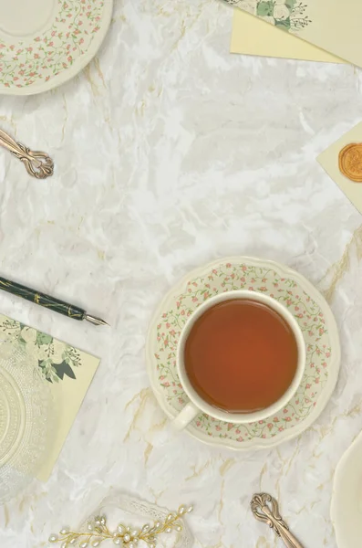 En üst görünüm çay fincanı ile zarif masa, içerik ve yazma araçları, zarflar, kalem, kartlar ile doldurulacak boş alan.