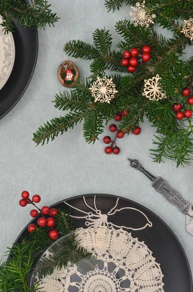 Noel yemeği için hazırlıklar: siyah tabaklar ve naneli masa örtüsü üzerine eski bir peçete. Evergreen dalları, kırmızı geleneksel dekorasyon ve ahşap kar taneleri. 