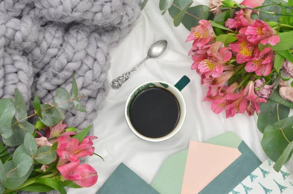 Rahat gri battaniye, sade kahve, pembe çiçekler, antika kaşık, kırtasiye ve boş kağıt. Blogcu için.