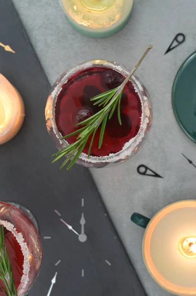 Kırmızı içkiler ve yeni yıl arifesi zamanı. Saat gece yarısına beş var. Dağılmış saat kolları, yanan mumlar ve iki içki. Sığ alan derinliği. 