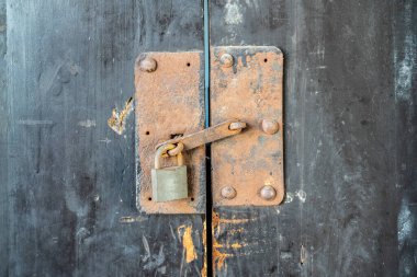 Eski ahşap bir kapıya asılı metal bir kilit.  