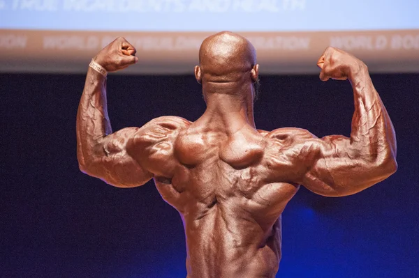 Mies kehonrakentaja taivuttaa lihaksiaan ja näyttää parhaan ruumiinsa — kuvapankkivalokuva