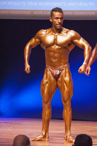 Mies kehonrakentaja taivuttaa lihaksiaan ja näyttää parhaan ruumiinsa — kuvapankkivalokuva