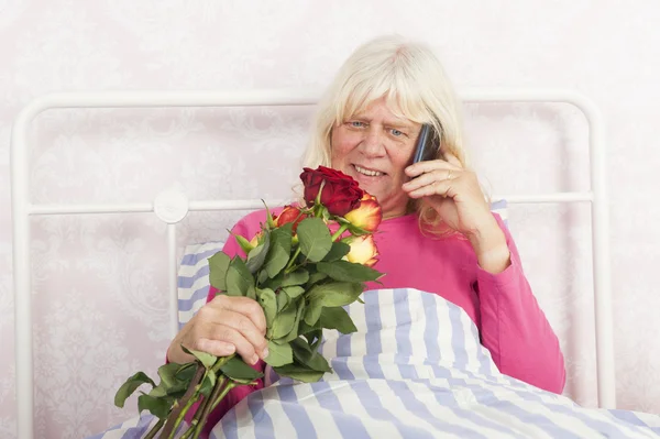 Kvinne i seng med roser og telefon – stockfoto