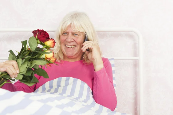 Mujer sonriente en la cama con rosas y teléfono — Foto de Stock