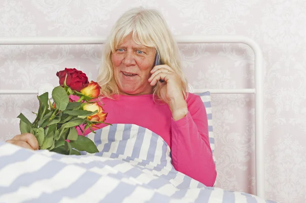 Cheerfull žena v posteli s růžemi a telefon — Stock fotografie