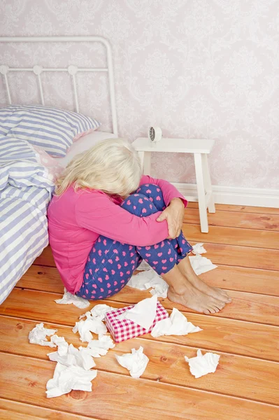 Sad woman sitting on floor next to bed — Stock Photo, Image
