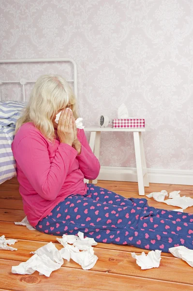 Sick woman sitting against bed — Stock Photo, Image