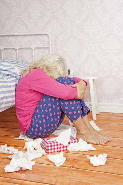 Sad woman sitting on floor against bed