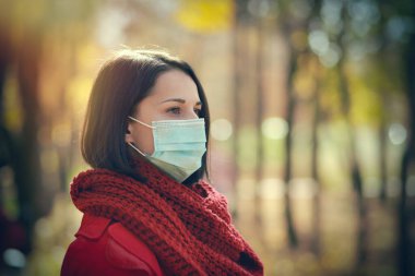 Sonbahar parkında tıbbi koruyucu maskeli güzel bir kadın dışarıda yürüyor. Coronavirus karantina konsepti