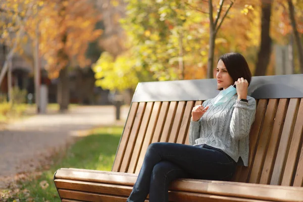 Schöne Junge Frau Medizinischer Schutzmaske Sitzt Auf Einer Bank Herbstpark — Stockfoto