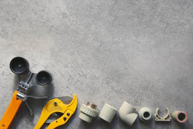 Büyük kopya alanı olan gri arka planda tesisat araçları. PVC ve pp plastik boru kaynaklama aracı. Sarı lehim, makas ve takılar..