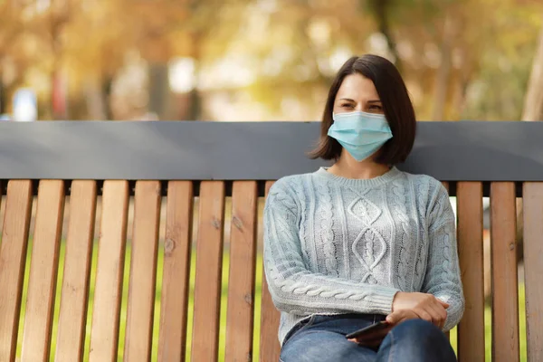 Schöne Junge Frau Medizinischer Schutzmaske Sitzt Auf Einer Bank Herbstpark — Stockfoto