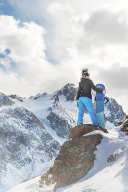 Karlı dağda kayanın tepesindeki snowboardcu kadın.
