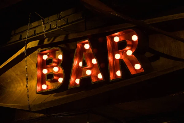 Grandes letras vermelhas luminosas perto do bar. Lâmpadas amarelas. — Fotografia de Stock