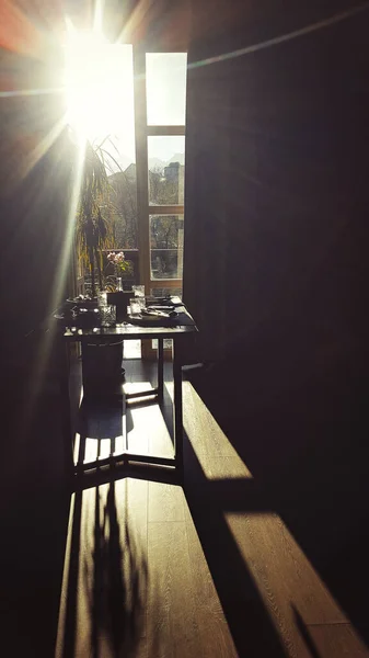 Tisch zum Frühstück in der Morgensonne durch ein französisches Fenster. Schatten und Sonnenstrahlen im dunklen Raum — Stockfoto