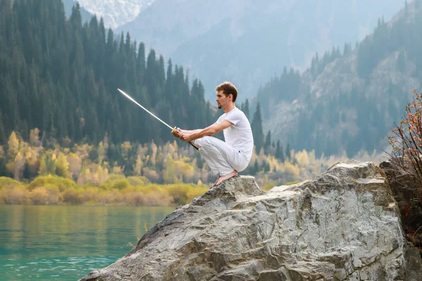 A barefoot man sits on a stone and holds a sword in his hands. Preparing for the battle. Man health concept