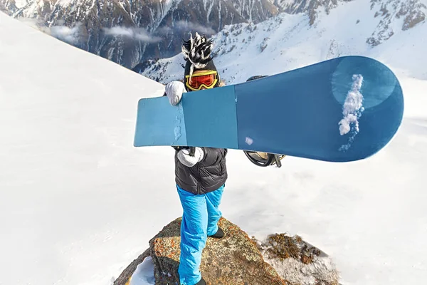 Snowboardos símaszkban és vicces kalap tartja kék snowboard előtt a kamera — Stock Fotó
