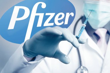 Koronavirüs COVID hastalığına karşı Pfizer Biontech aşısı. Şırınga doktorun elinde ve logo Pfizer arka planda.
