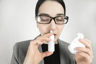 Gözlüklü genç kadın, burun spreyi kullanıyor.
